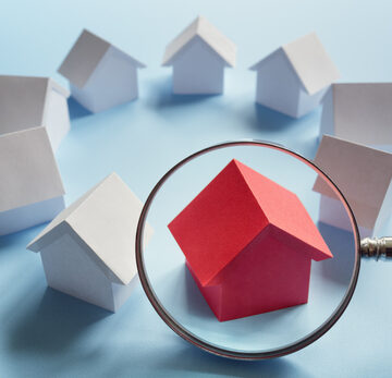 Concept Image Of Choosing A Home With A Circle Of White Toy Houses And One Red House Under A Magnifying Glass