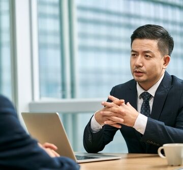 Two Asian Business Men Sitting At A Desk Face To Face