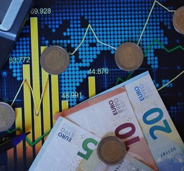 Eurozone Banknotes And Coins Sitting Atop Graphs And Stock Charts