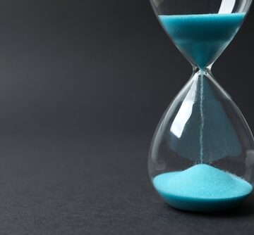 Modern Hourglass On Black Background With Sand Running Through The Glass