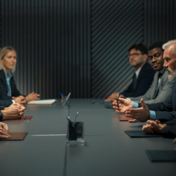 Conference Room Table Lined With Smiling, Suited Male And Female Executives