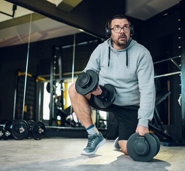 Overweight Middle-Aged Man Training With Dumbbells In The Gym