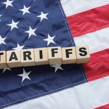 Import Trade Concept With U.S. Flag And Wooden Blocks Spelling "Tariffs"
