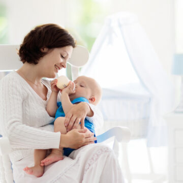 Mother In Rocking Chair Feeding Her Newborn Baby With A Bottle