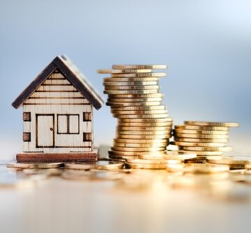 A Model House Next To Some Wobbly Stacks Of Coins