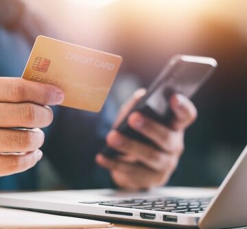 Close Up Of Male Hands Holding A Credit Card And Smartphone Sitting At A Laptop