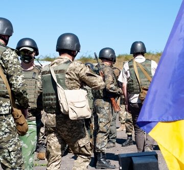 A Group Of Armed Ukrainian Soldiers Gather Near The Flag Of Ukraine