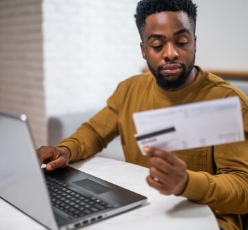 Young,Man,Using,Credit,Card,And,Laptop,For,Paying,Bills A Young Man Using A Credit Card And Laptop For Paying Bills