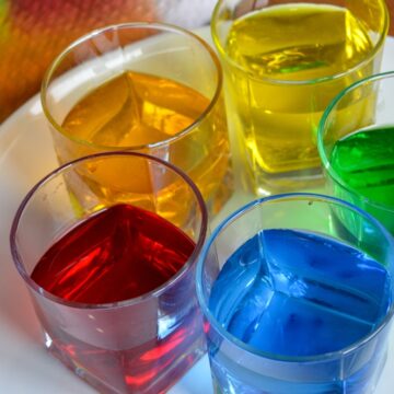 Five Glasses Filled With Vividly Colored Liquids Of Red, Blue, Green, Yellow, And Orange