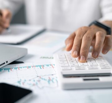 Business Accounting Concept With Businesswoman Hand Using Calculator, Graphs, Laptop, And Notebook