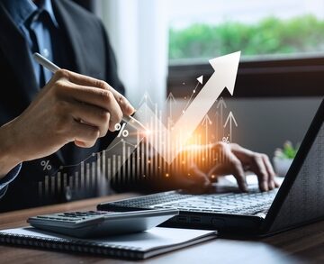 Business, Finance, And Investment Image Of Businessman With Computer And Calculator With Upward Graph Digitally Superimposed