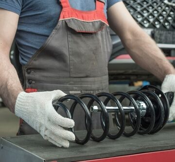 An,Auto,Mechanic,Holds,A,New,Shock,Absorber,Strut,And An Auto Mechanic Holds A New Shock Absorber Strut And Coil