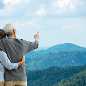 Senior Asian Couple Hugging And Pointing At Mountainous Landscape