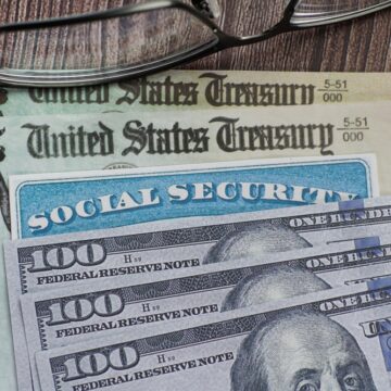 U.S. Treasury Bonds, A Social Security Card, And $100 Bills Laid Out With Reading Glasses
