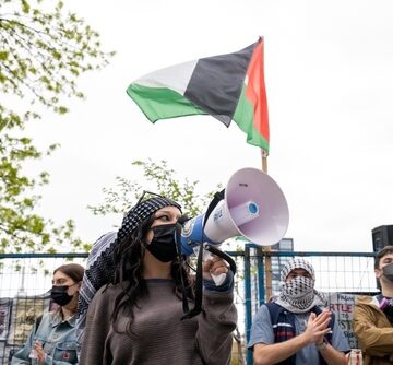 A Pro-Palestine Rally The Palestinian Flag And Demonstrators Holding Signs And Using A Megaphone