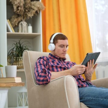 A Man With Headphones Deeply Immersed With His Tablet