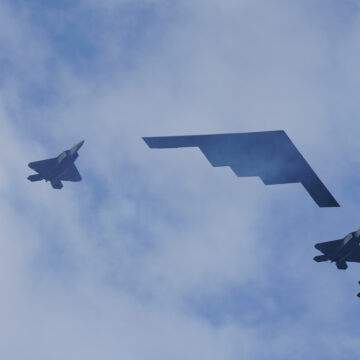 A Formation Flight Featuring A Northrop Grumman B-2 Spirit Stealth Bomber, Flanked By Four F-22 Raptor Jets