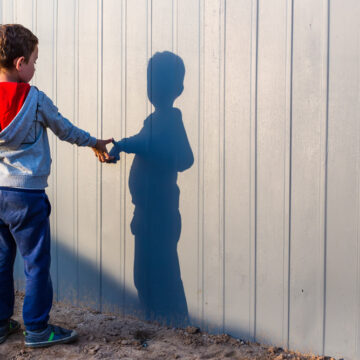 A Boy Touching His Shadow On A Grey Painted Fence