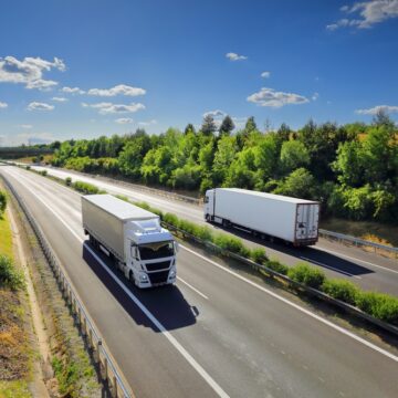 Cargo Trucks Passing On Opposite Sides Of Forest-Lined Highway