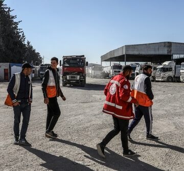 Aid Workers Walking Toward Trucks Loaded With Humanitarian Aid And Supplies To Enter Through The Kerem Shalom Border Crossing