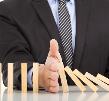 Photo Of A Businessman's Hand Stops Falling Dominoes