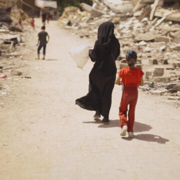 A Palestinian Mother And Daughter Walk Along A Rubble-Strewn Road