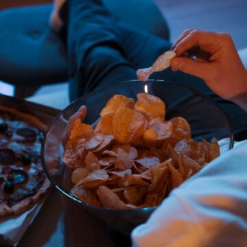 Man Eating Chips And Pizza While Watching TV While Sitting On A Sofa