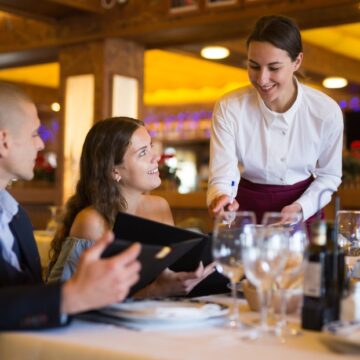 A Female Waitperson Pouring Water For A Young Couple In A Fancy Restaurant