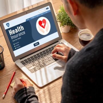 Image Shows A Person Looking At A Laptop Screen Displaying A "Health Insurance" Web Page