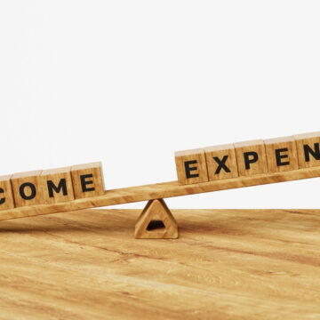 Wooden Blocks Spelling The Words "Income" And "Expenses" On A Seesaw, Tipping Down Toward "Income"