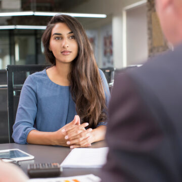 Young, Focused Woman Sitting Across The Desk From Businessman In Suit