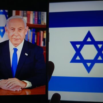 Israeli Prime Minister Benjamin Netanyahu Sitting At A Desk Next To A Large Flag Of Israel