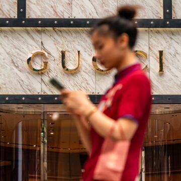 A Young Asian Shopper Walking Past A Gucci Store In Chongqing, China