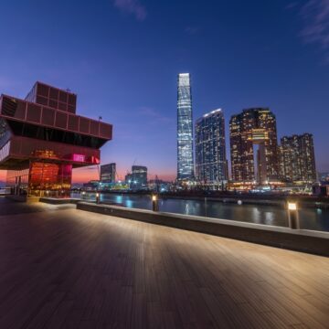 Image Shows The West Kowloon Cultural District In Hong Kong Taken From The Waterfront Promenade, With The Victoria Harbour And The Hong Kong Island Skyline In The Background