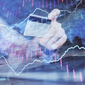 Double Exposure Of Hands Holding A Credit Card Over A Laptop Keyboard, Overlaid With Financial Charts And A World Map