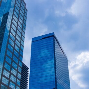 The Image Shows A Cityscape Of Moving Clouds Reflecting Modern, Glass-faced Office Buildings