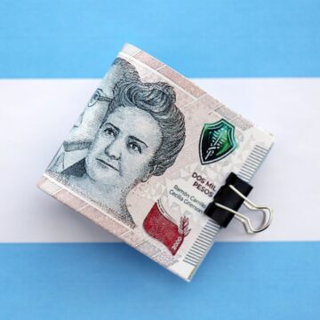An Image Of The 2,000 Argentine Peso Banknote In A Clip Sitting Atop The Argentinian Flag