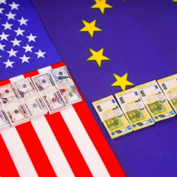 Miniature Replicas Of U.S. Dollar And Euro Banknotes Set Against The Flags Of The United States And The European Union