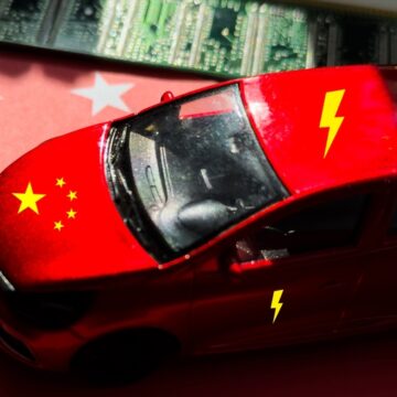 Concept Image For China's Electric Vehicles With A Red Toy Car With The Chinese Flag On Its Hood And Lightning Bolts On Its Roof, A Computer Motherboard, And The Chinese Flag On The Car And Background