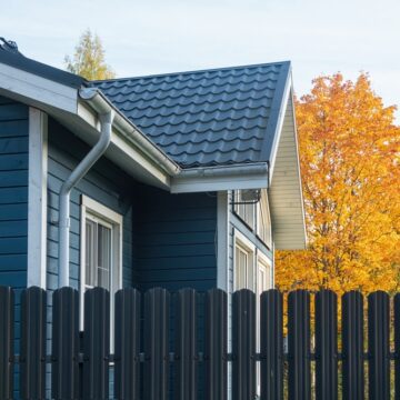 A One-Story Blue Wooden Residential Building Behind A Dark Metal Fence In The Foreground