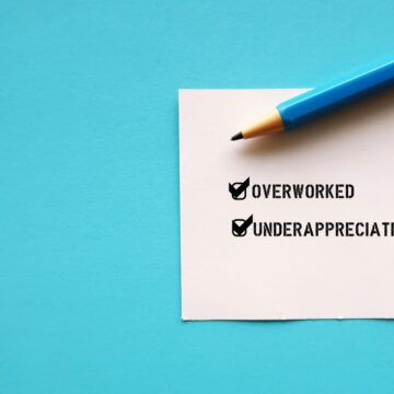 An Office Post-it Note On Blue Background With Two Items Checked Off: "OVERWORKED" And "UNDERAPPRECIATED"