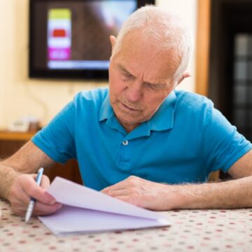 A White-haired Elderly Man Is Focused On Reviewing Documents At A Table