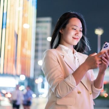 A Young Woman Using A Smartphone On A Bustling Street In Hanoi At Night