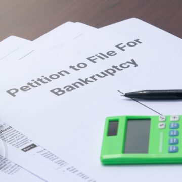 Image Shows A "Petition to File For Bankruptcy" Form Along With A Pen And Calculator