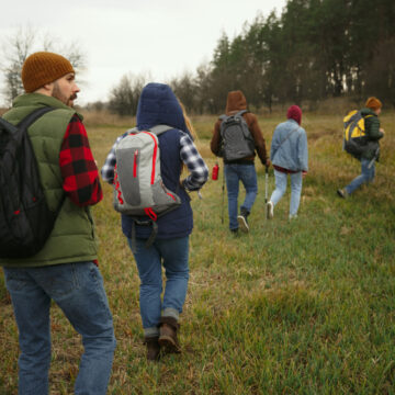 A Group Of Young People Hiking Or Backpacking And Walking Along A Grassy Trail In A Field