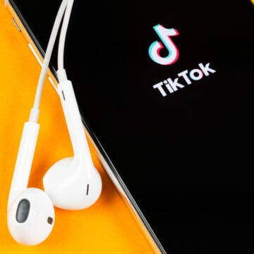 The TikTok Logo On A Mobile Phone Next To A Pair Of AirPods