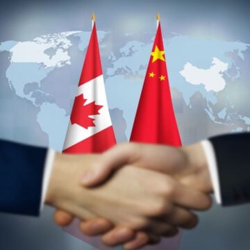 Concept Image Representing Diplomatic Engagement Between Canada And China Relations With Two Men Shaking Hands With The Canadian And Chinese Flags And World Map In The Background
