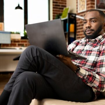 A Man Using A Laptop In A Home Office Working Remotely But Staring Off Into Space