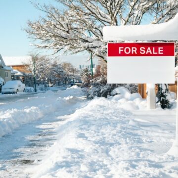 Home With A Red And White "For Sale" Sign In A Snow-covered Suburban Neighborhood