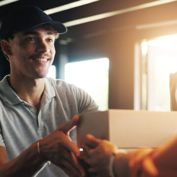 A Smiling Delivery Man Handing A Small Cardboard Box To The Likely Recipient